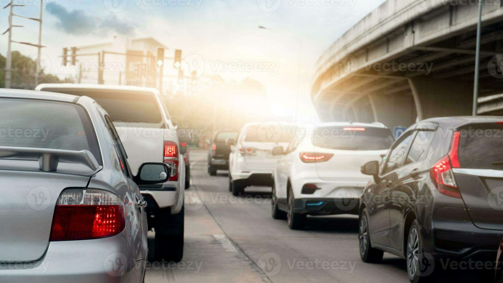 Rear side of car on the road with many cars queue up from the traffic lights. Beside with bridge made from cement. Background of bright orange and sky. photo