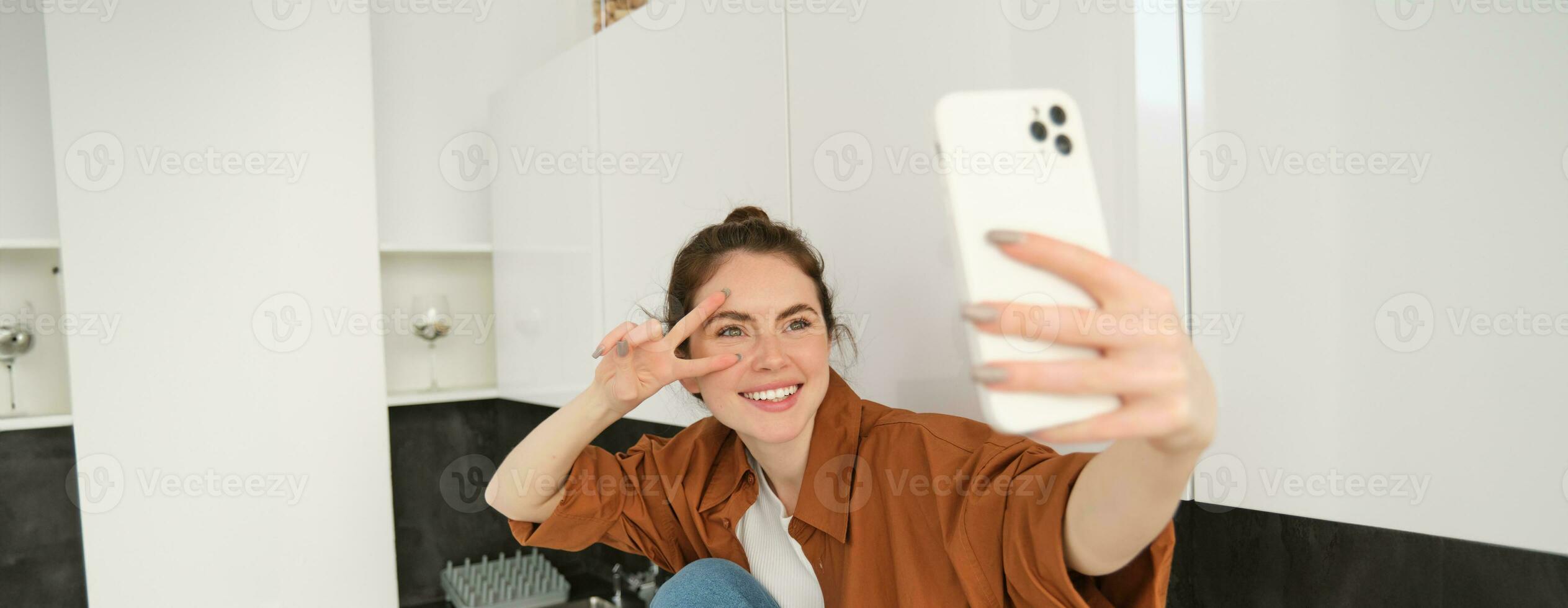 Portrait of beautiful young woman takes selfie on her smartphone, posing for photos, using filter app to take pictures for herself photo