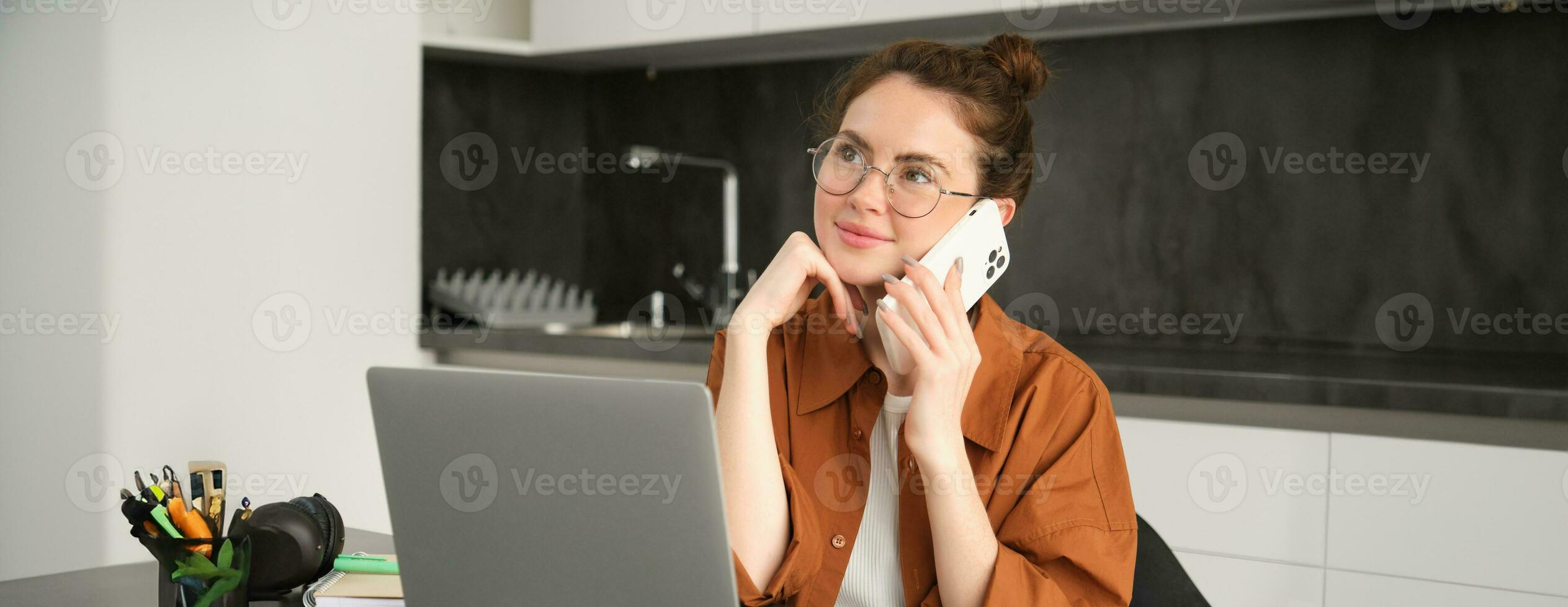 Portrait of young selfemployed woman, entrepreneur working from home, freelancer calling client. Girl making an order, talking to someone on phone, sitting in kitchen with laptop photo