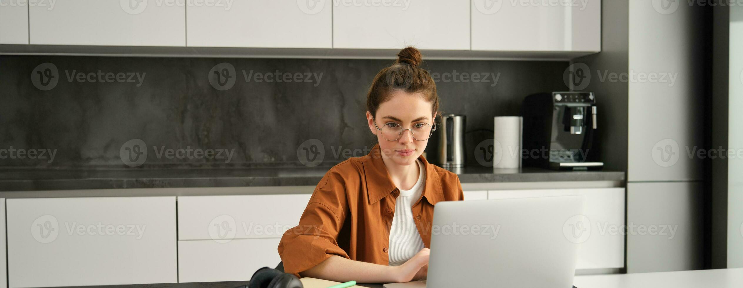 Work and life balance concept. Young woman in glasses, working from home, typing on laptop, student doing homework on computer, sitting in kitchen, freelancing photo