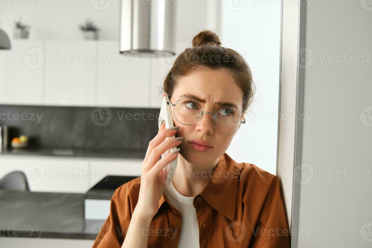 Portrait of woman with disappointed face, standing at home, answers phone call with concerned face, has difficult telephone conversation photo