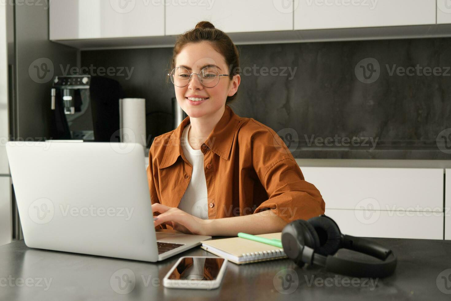 Portrait of smiling cute woman in kitchen, freelancer working from home on laptop, digital nomad freelancing from home, typing on computer photo