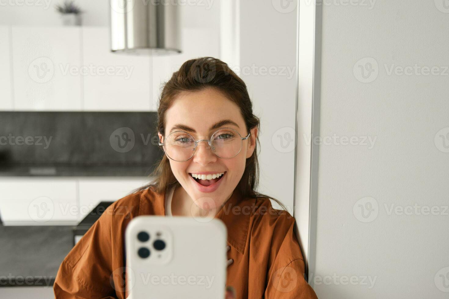Close up portrait of happy girl takes selfie on smartphone, posing with mobile phone, looking excited and amazed, smiling at telephone camera, using social media app photo