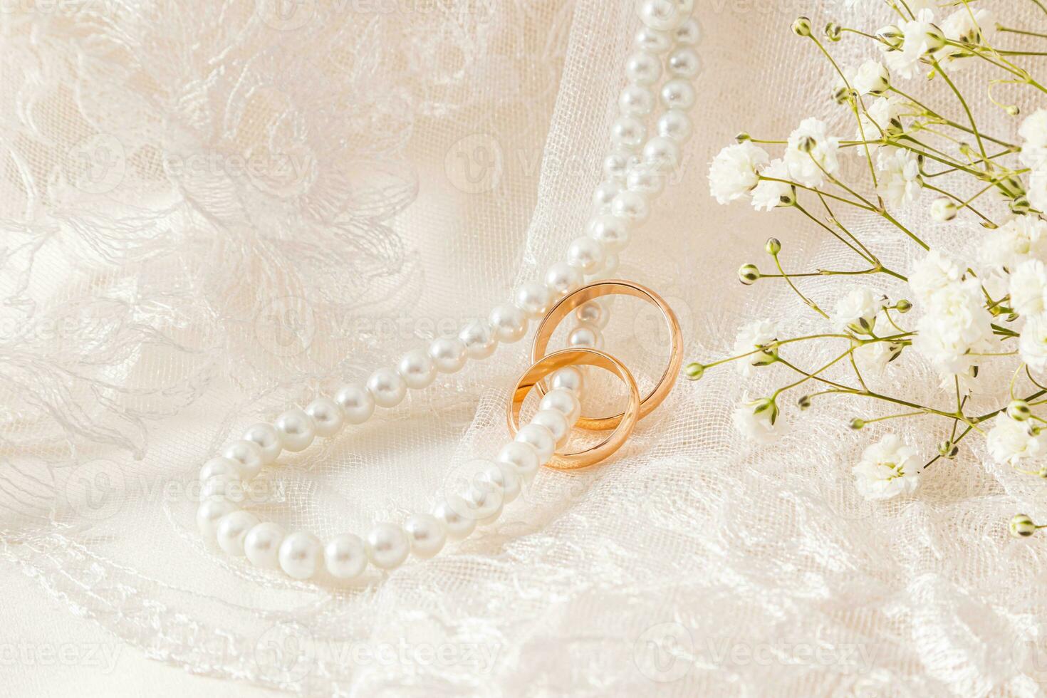 Retro beige tulle and long pearl beads hang along the soft folds of fabric with gold wedding rings worn on them. A copy space. mockup photo