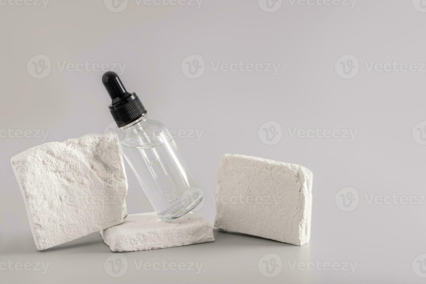 A beautiful transparent bottle with a pipette with an enhancering cosmetic product leaned on a white brick slice. Natural cosmetics. Front view. photo