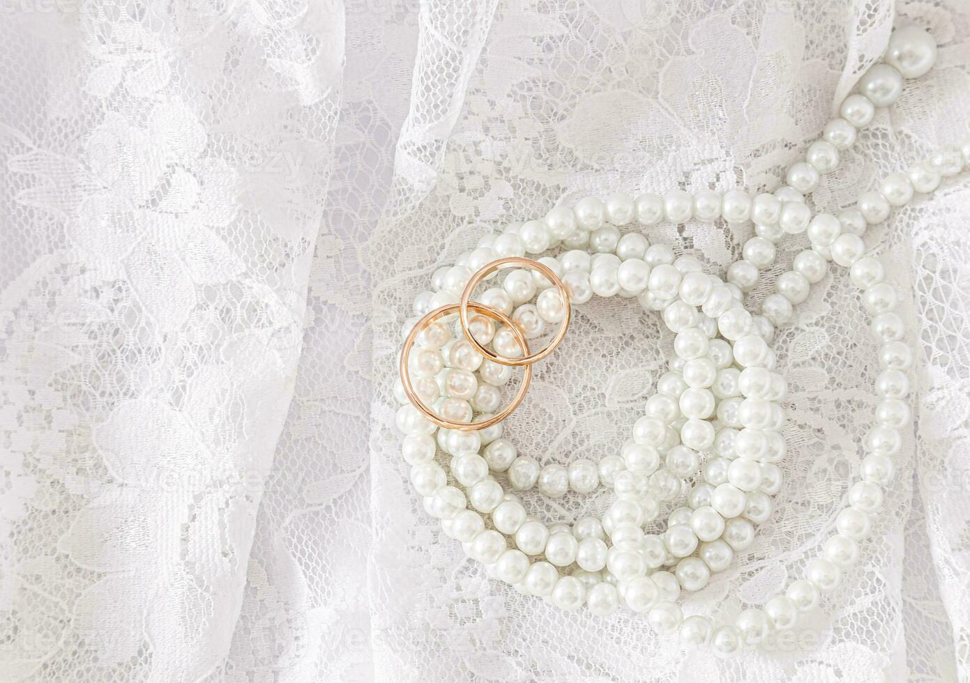 Two gold wedding rings lie on a luxurious vintage part of the bride's wedding dress with a string of pearl beads. Wedding concept. Top view. photo