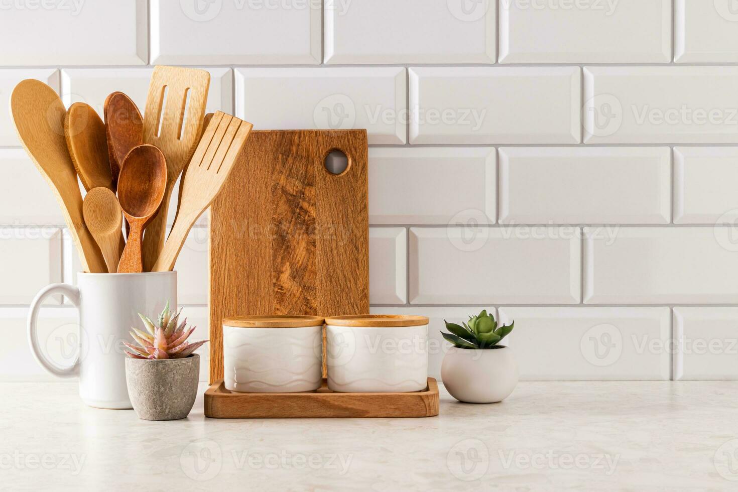 Ceramic white jars, wooden spoons in potstav and wooden cutting board on kitchen light countertop. Front view. A copy of the space. Eco style. photo