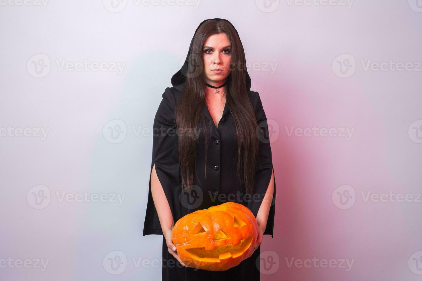 Woman as witch is standing with the pumpkin in the studio. Halloween and carnival concept photo