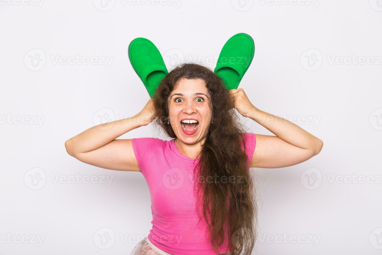 Pretty young woman fooling around with green slippers on white background photo
