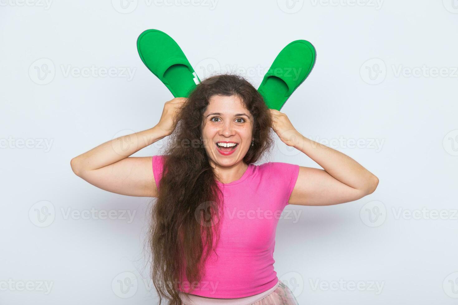 Pretty young woman fooling around with green slippers on white background photo