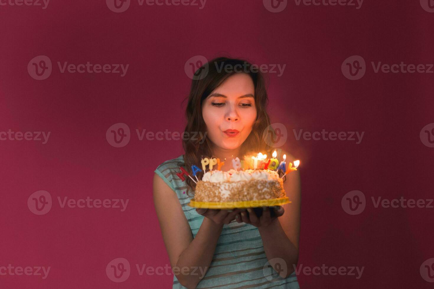 joven mujer soplo fuera velas en un cumpleaños pastel terminado rojo antecedentes. foto