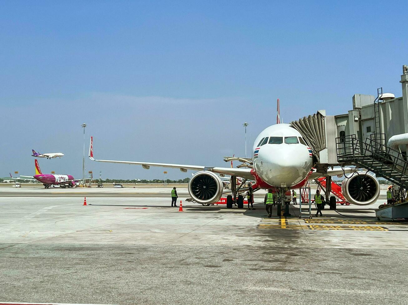 Bangkok, TH, 2022 - view of outside terminal Suvarnabhumi International Airport with Thai airplane arrives and parked delivers passenger with jet bridge under bright blue sky. photo