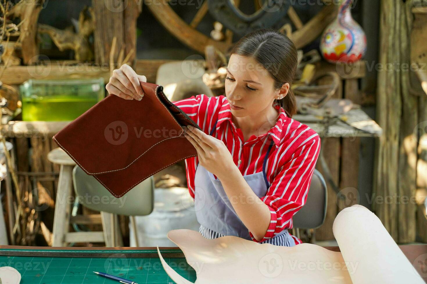 joven hembra cuero bienes fabricante mirando y cheque el pulcritud de el cueros bolso antes de vender a cliente en taller. foto