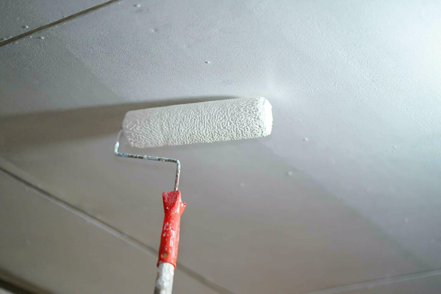 Closeup a painted roller is painted white on the ceiling of the house. photo