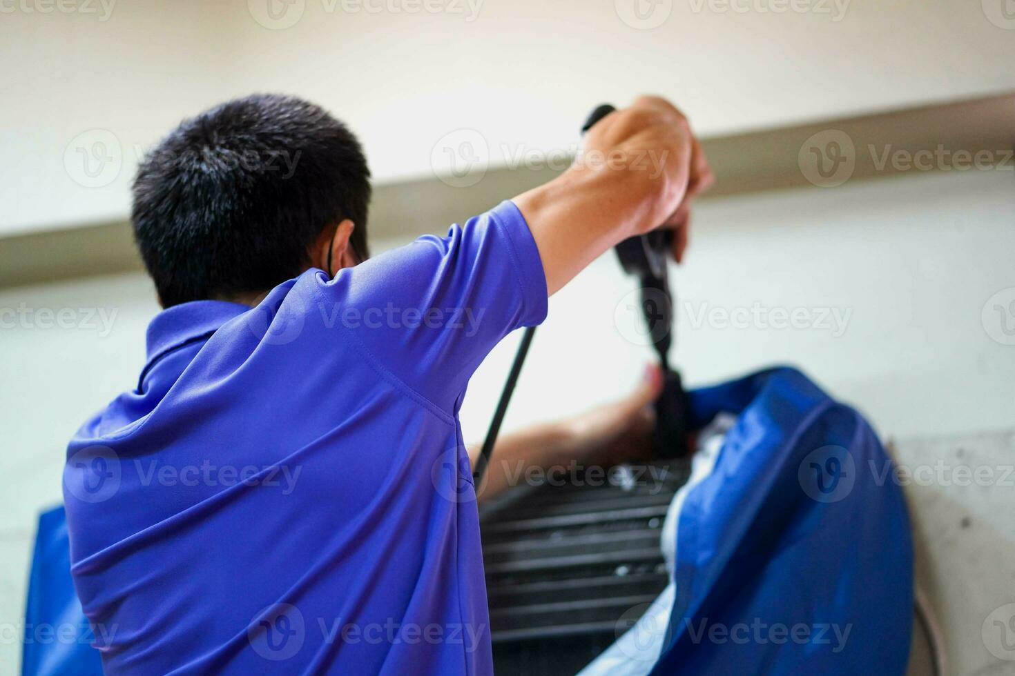 Closeup and crop electric repair technician holding water gun atomizer washing home's air conditioner coil cooler in the bedroom. photo