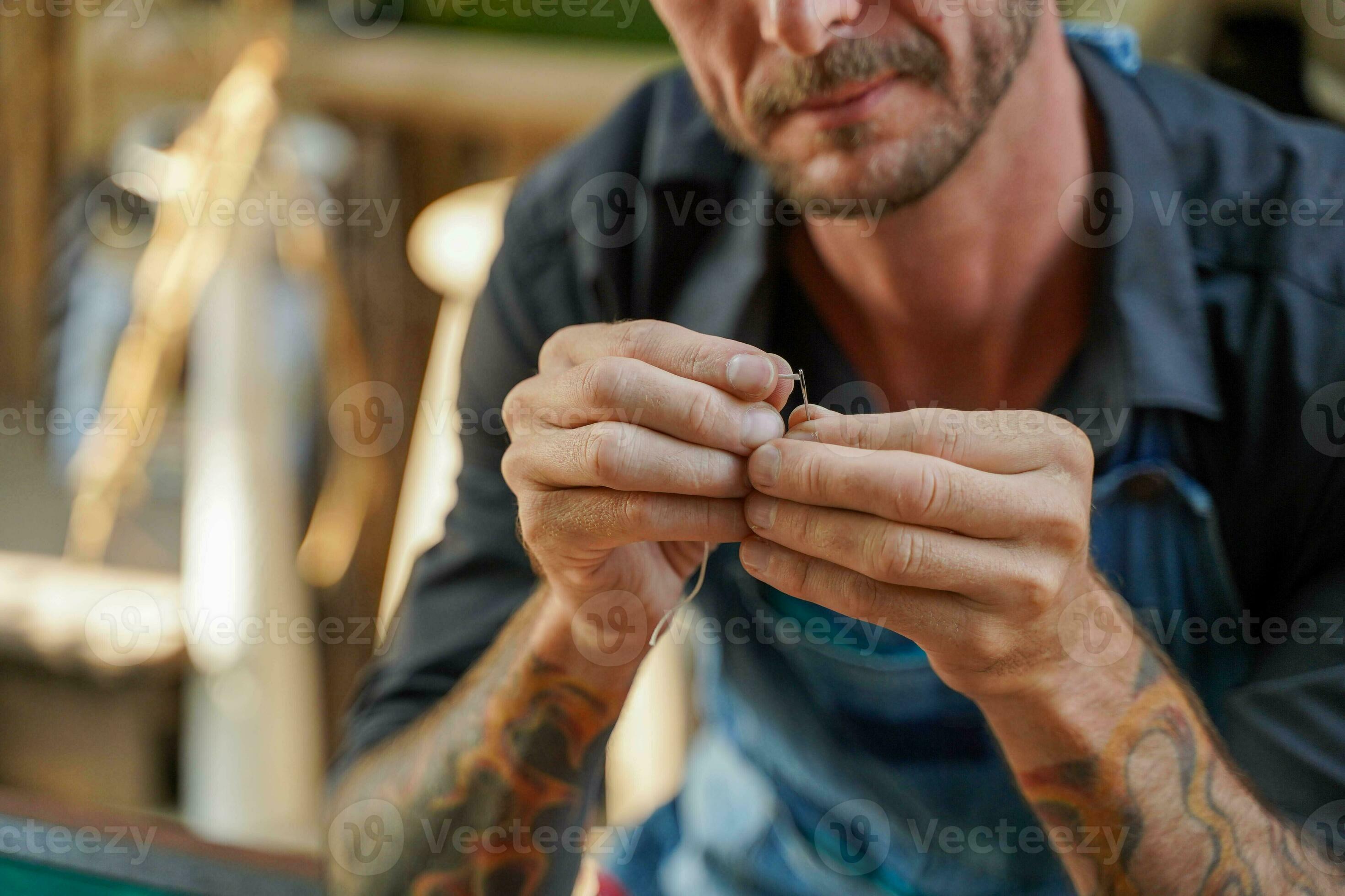 Closeup hand of leather craftsman is carefully threading a needle to