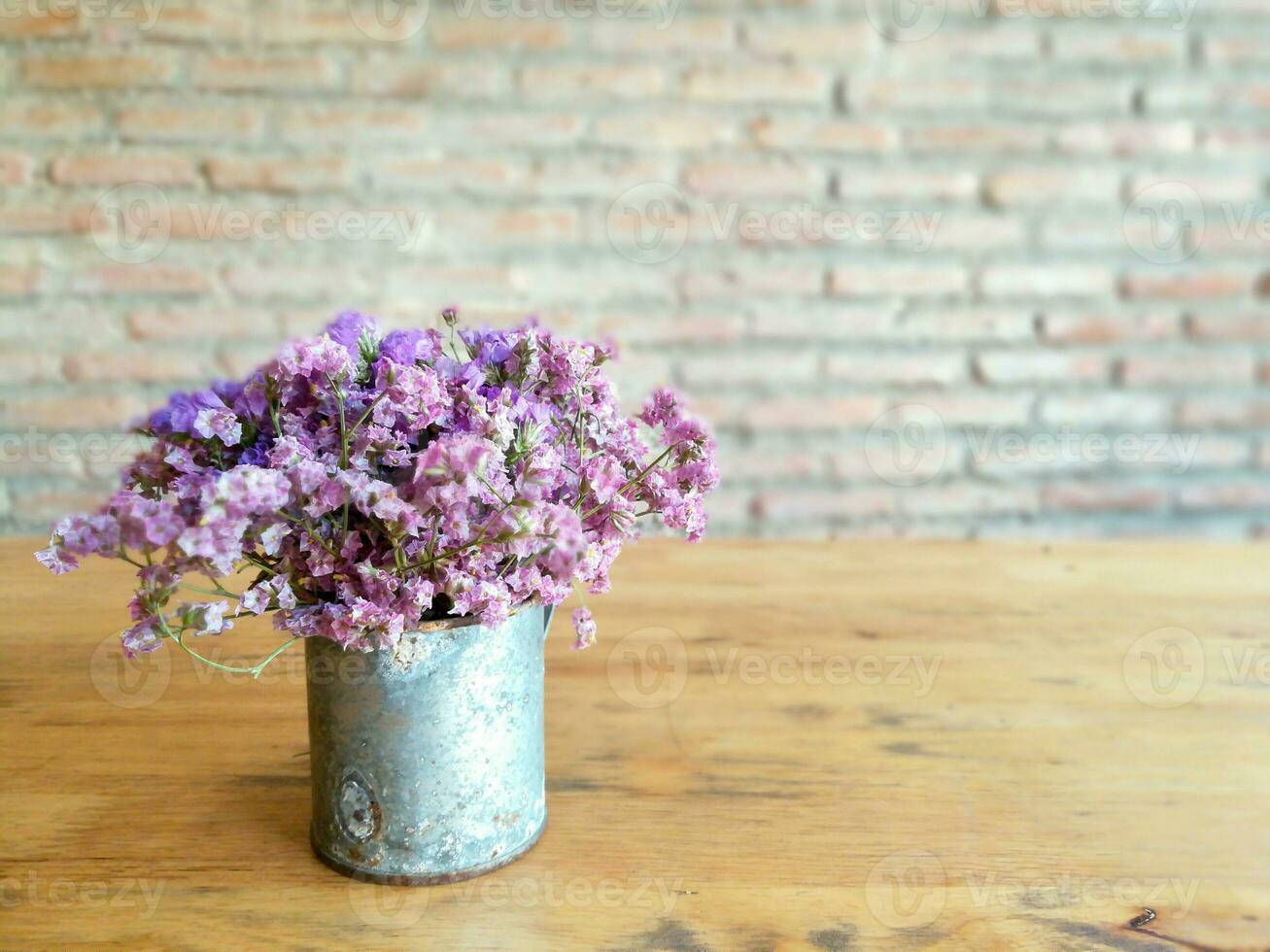 Beautiful violet flowers in zinc vintage vase on wooden table and old brick wall background. photo