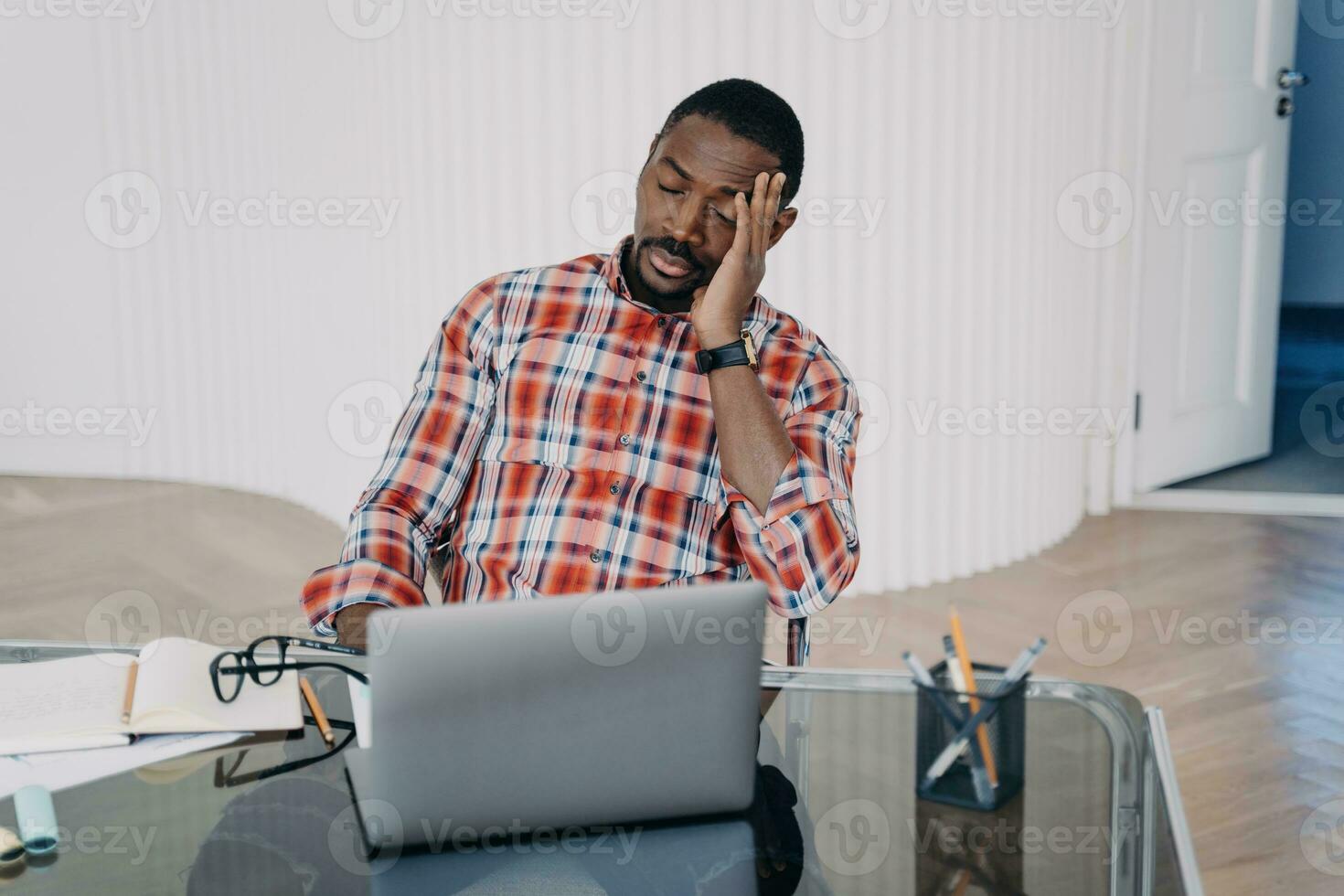 Stressed Black man at desk with laptop, feeling overwhelmed with work. photo