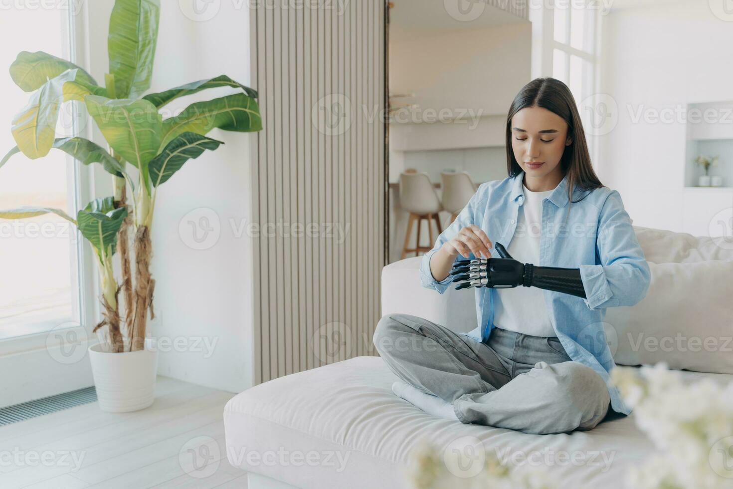 Serene woman with a bionic arm comfortably sits at home, showcasing harmony between technology and daily life photo