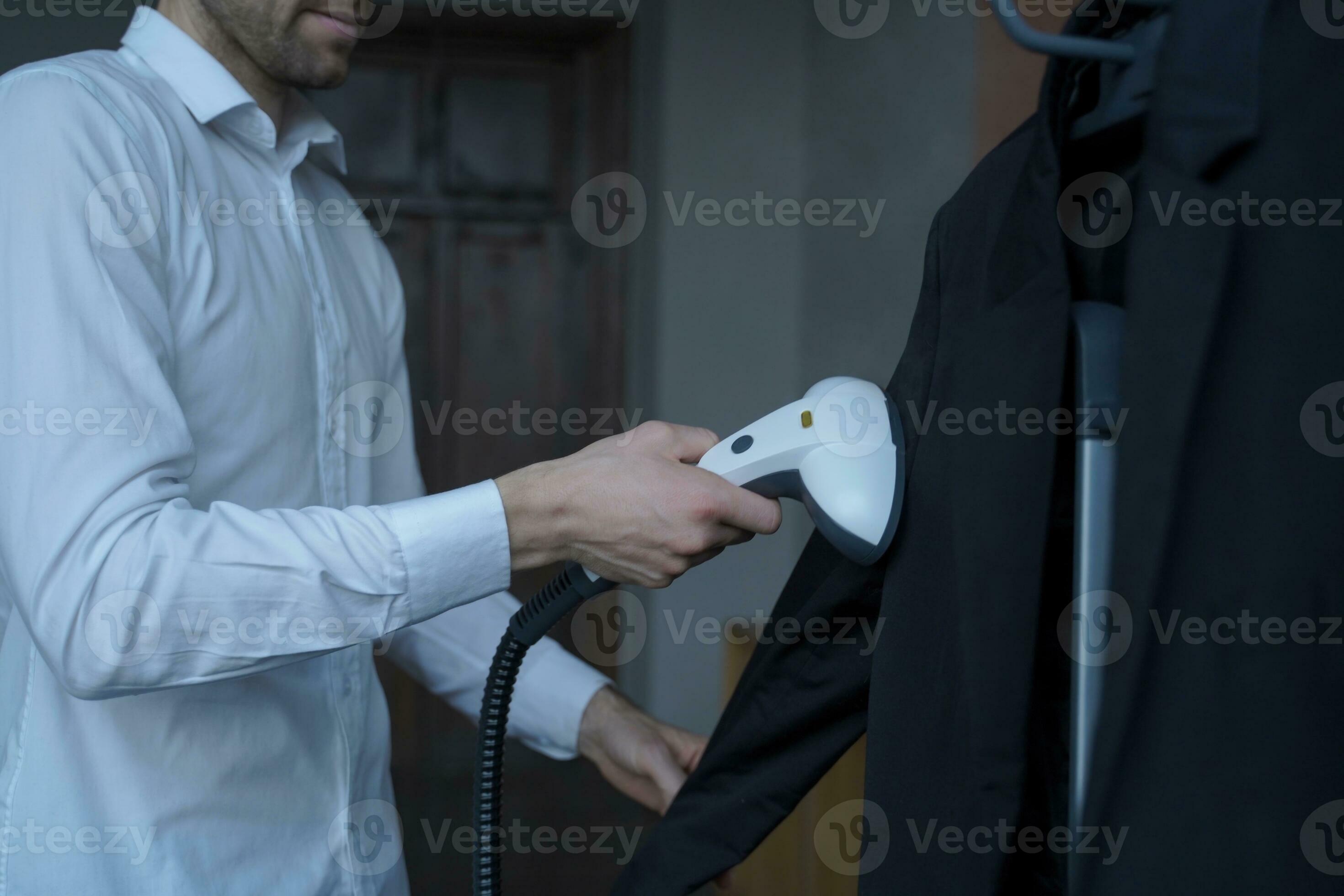 Focused man steaming a suit jacket, meticulous clothing care at home ...