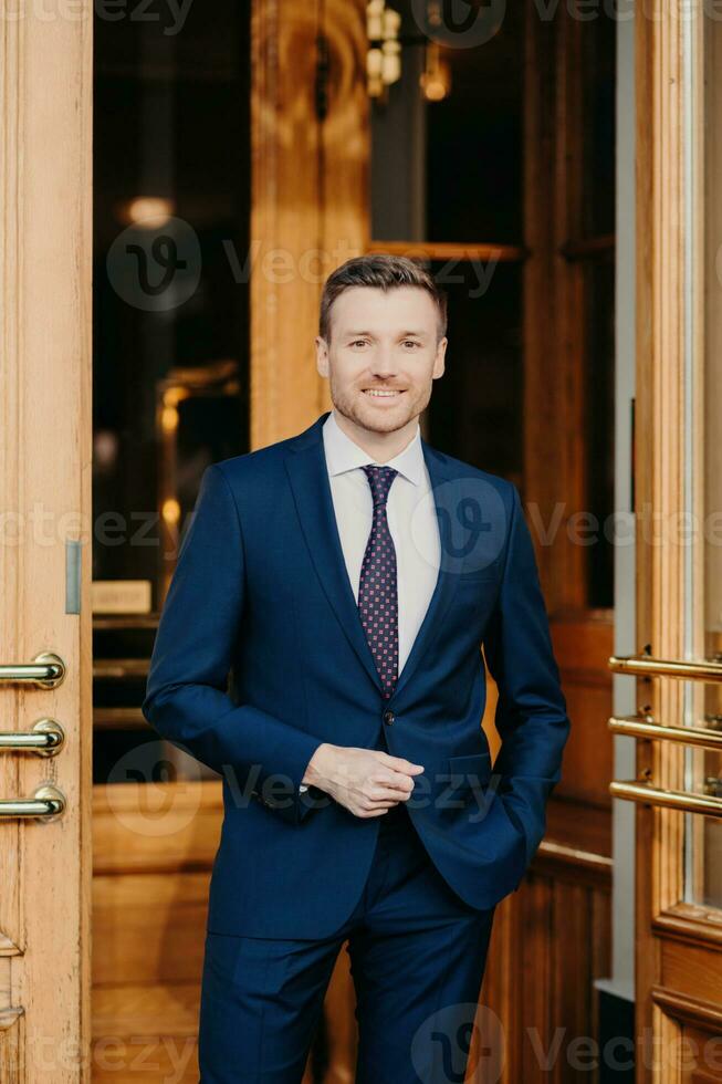 Smartly dressed man in a tailored blue suit and tie standing confidently in front of a luxury establishment photo