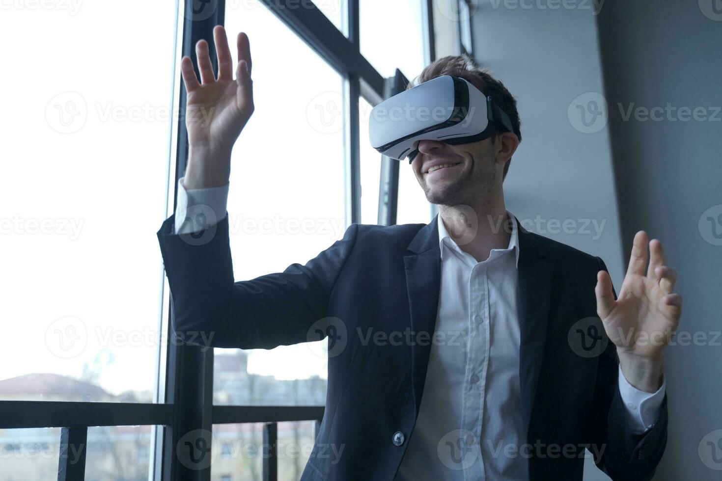 Smiling man in suit with VR headset, gesturing with raised hands photo