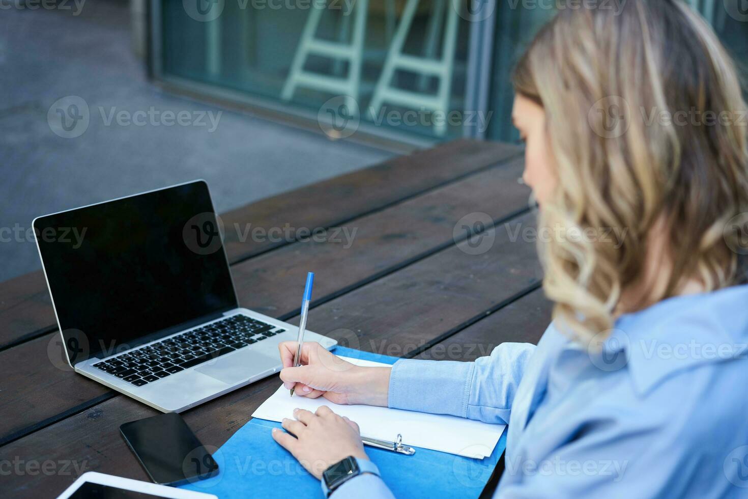 Close up portrait of woman student attend online course classes, sitting outside on fresh air with laptop and taking notes. Businesswoman video chat on computer photo