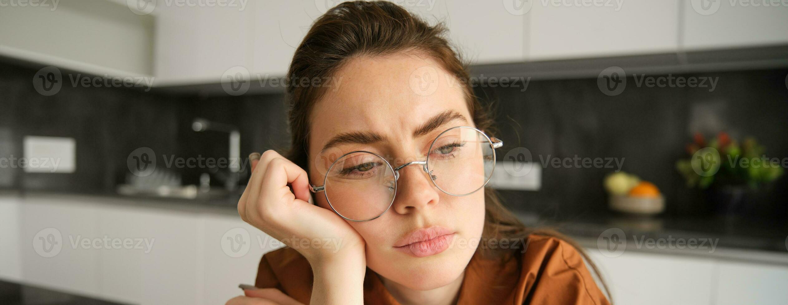 Close up portrait of woman in glasses with concerned, sad face, looking upset, troubled expression, sitting at home photo