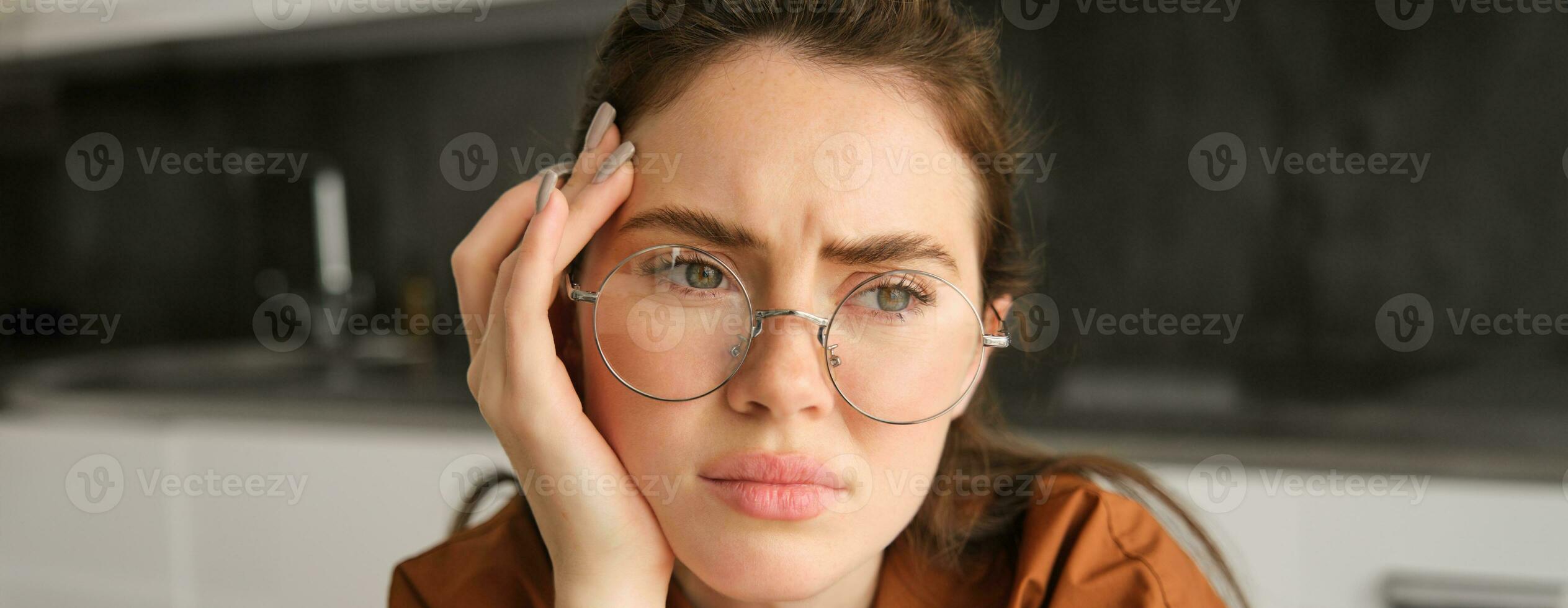 Close up portrait of woman in glasses with concerned, sad face, looking upset, troubled expression, sitting at home photo