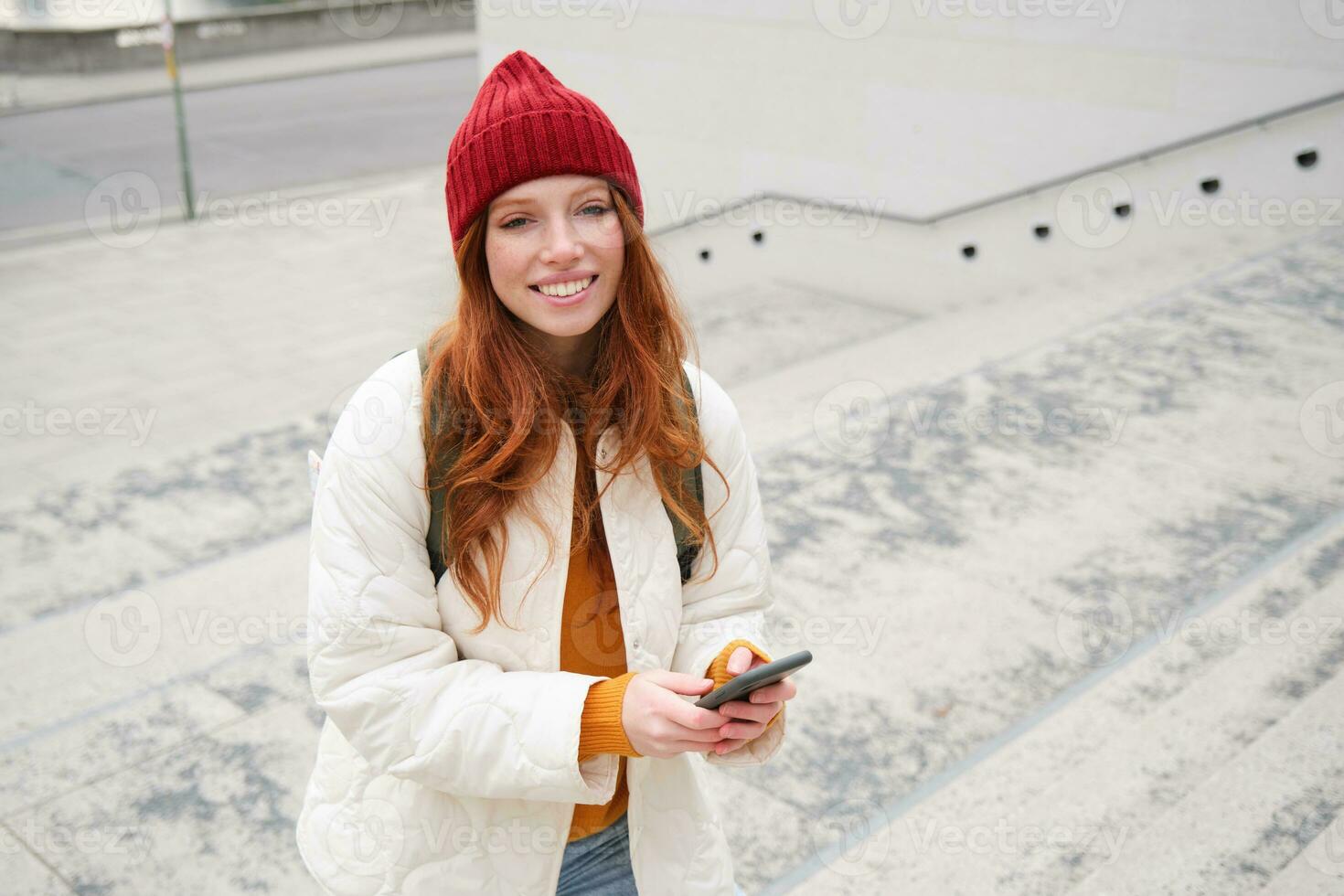 Smiling redhead girl, student tourist walks around city, goes up the stairs, looks at mobile phone map to get around town, sends message on smartphone photo