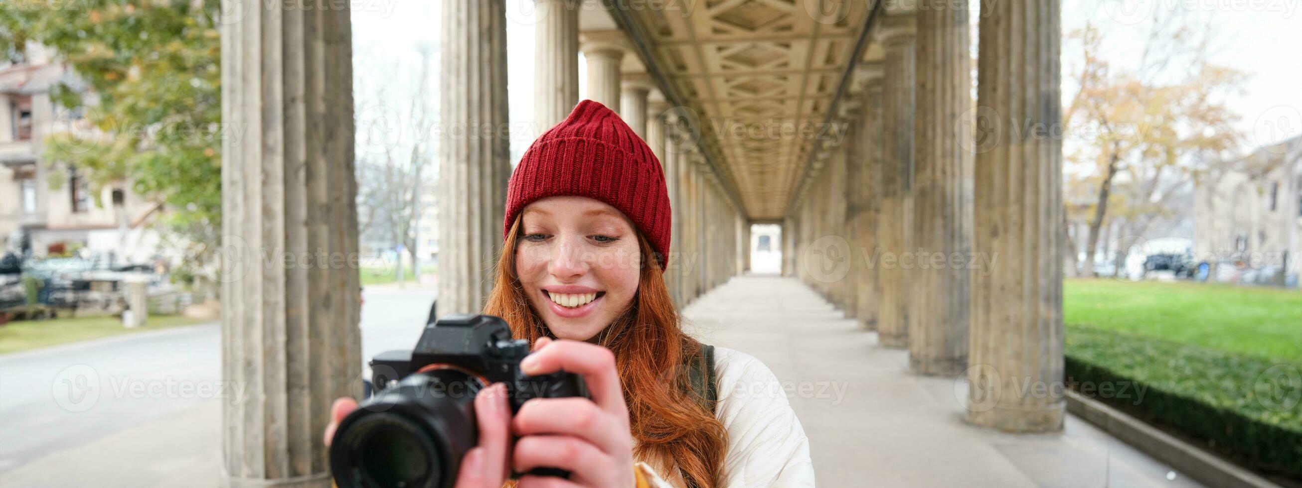 Smiling tourist photographer, takes picture during her trip, holds professional camera and makes photos
