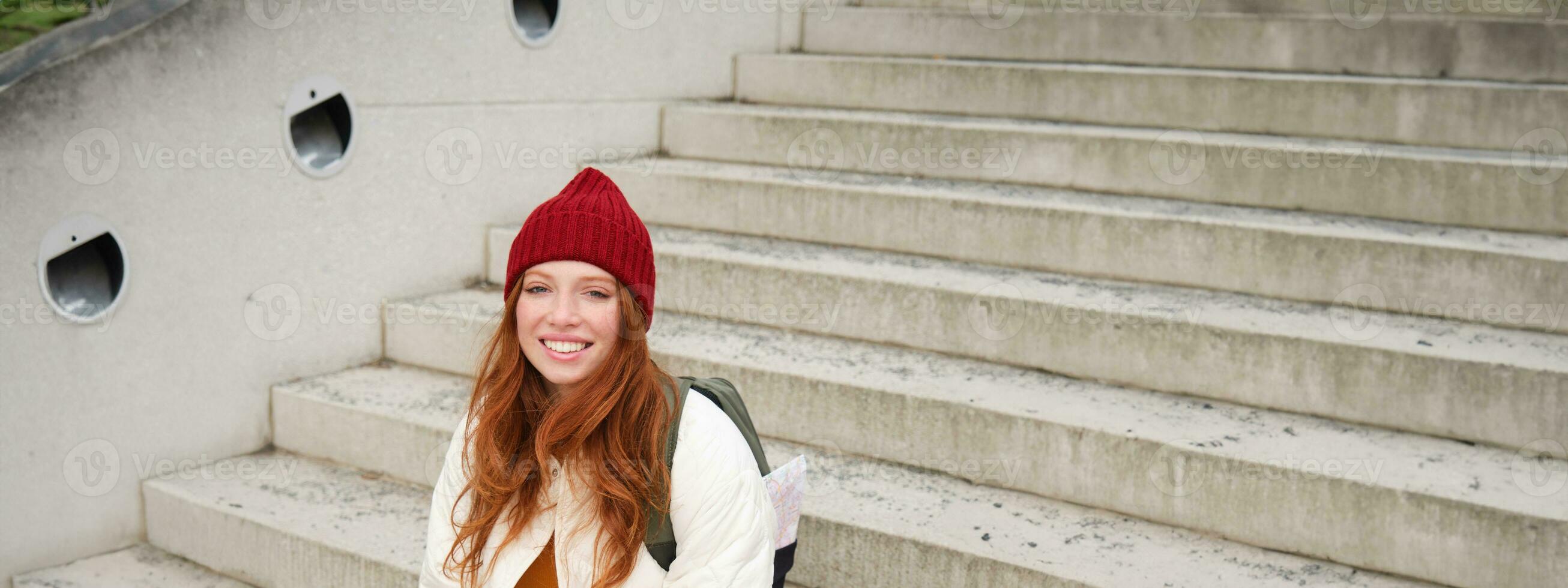 Smiling redhead girl, student sits on stairs outdoors and uses laptop, connects to public wifi in city and works on project, uses internet on computer photo