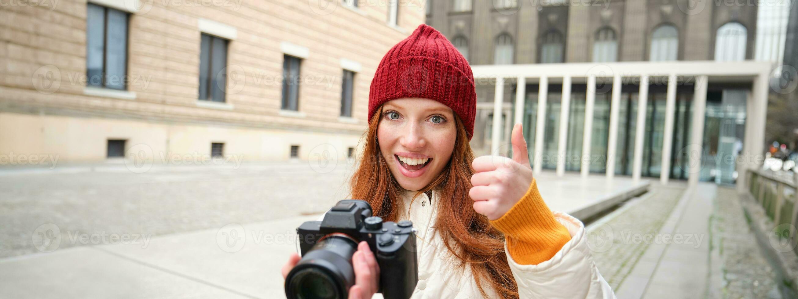 Beautiful readhead girl, photographer with professional camera takes pictures outdoors, walking around city and taking photos, sightseeing photo