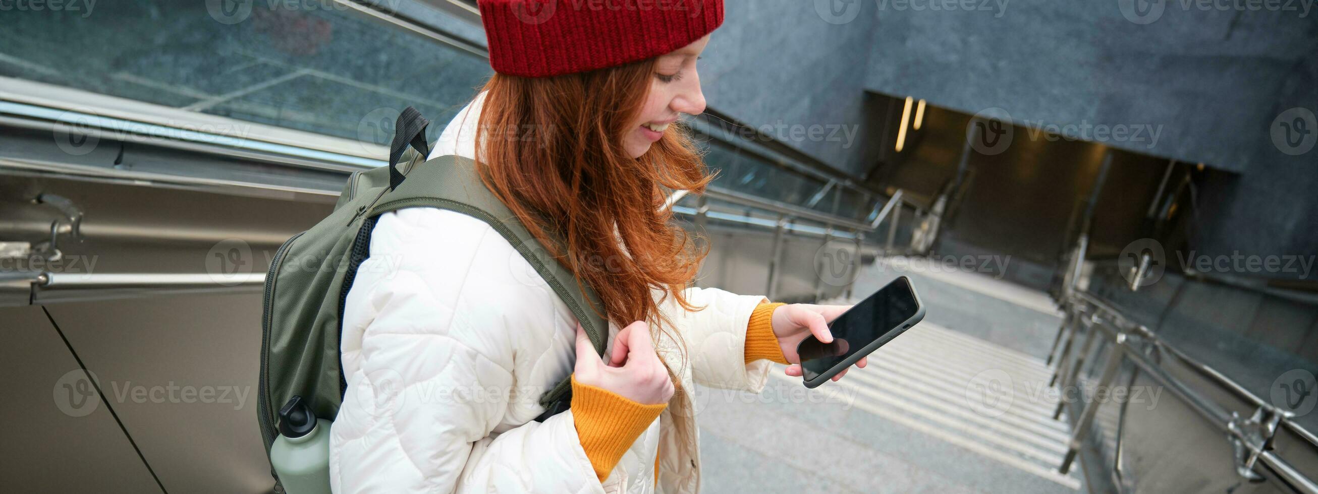 Smiling girl walking on stairs, using mobile phone, texting message on her way, using smartphone app map, follows route to destination place photo