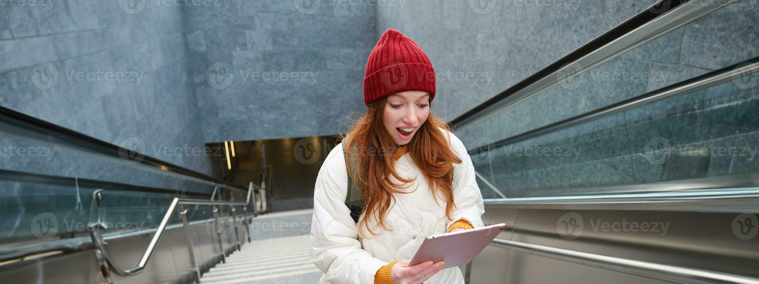 retrato de niña alumno, camina arriba escalera desde subterraneo y mira a digital tableta con conmocionado, sorprendido cara expresión, leyendo increíble Noticias foto