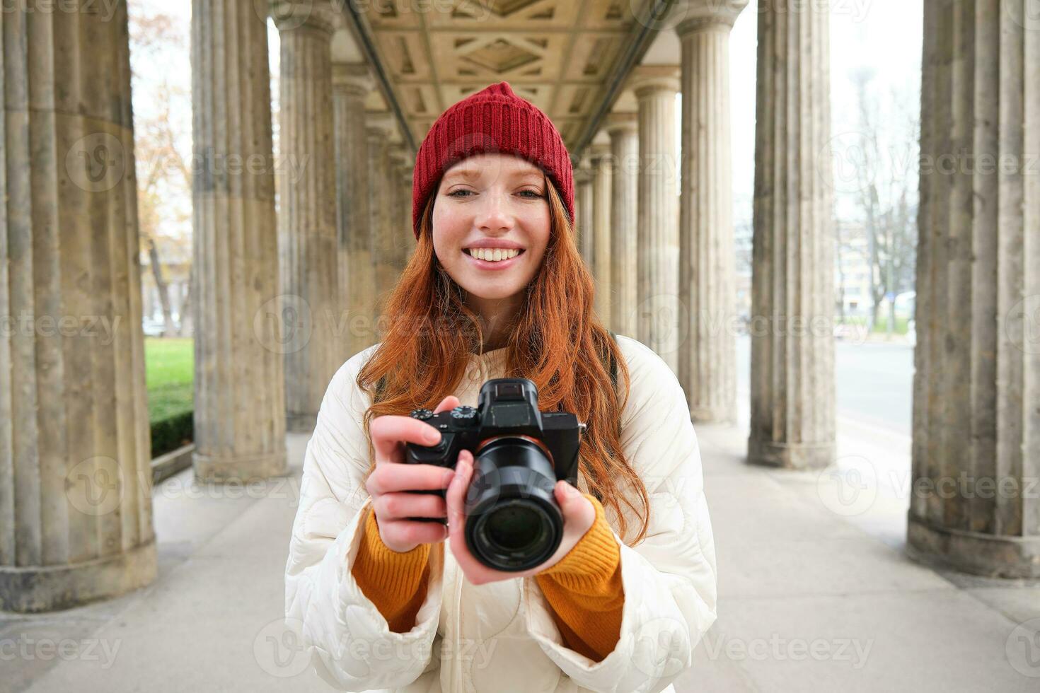 Smiling tourist photographer, takes picture during her trip, holds professional camera and makes photos