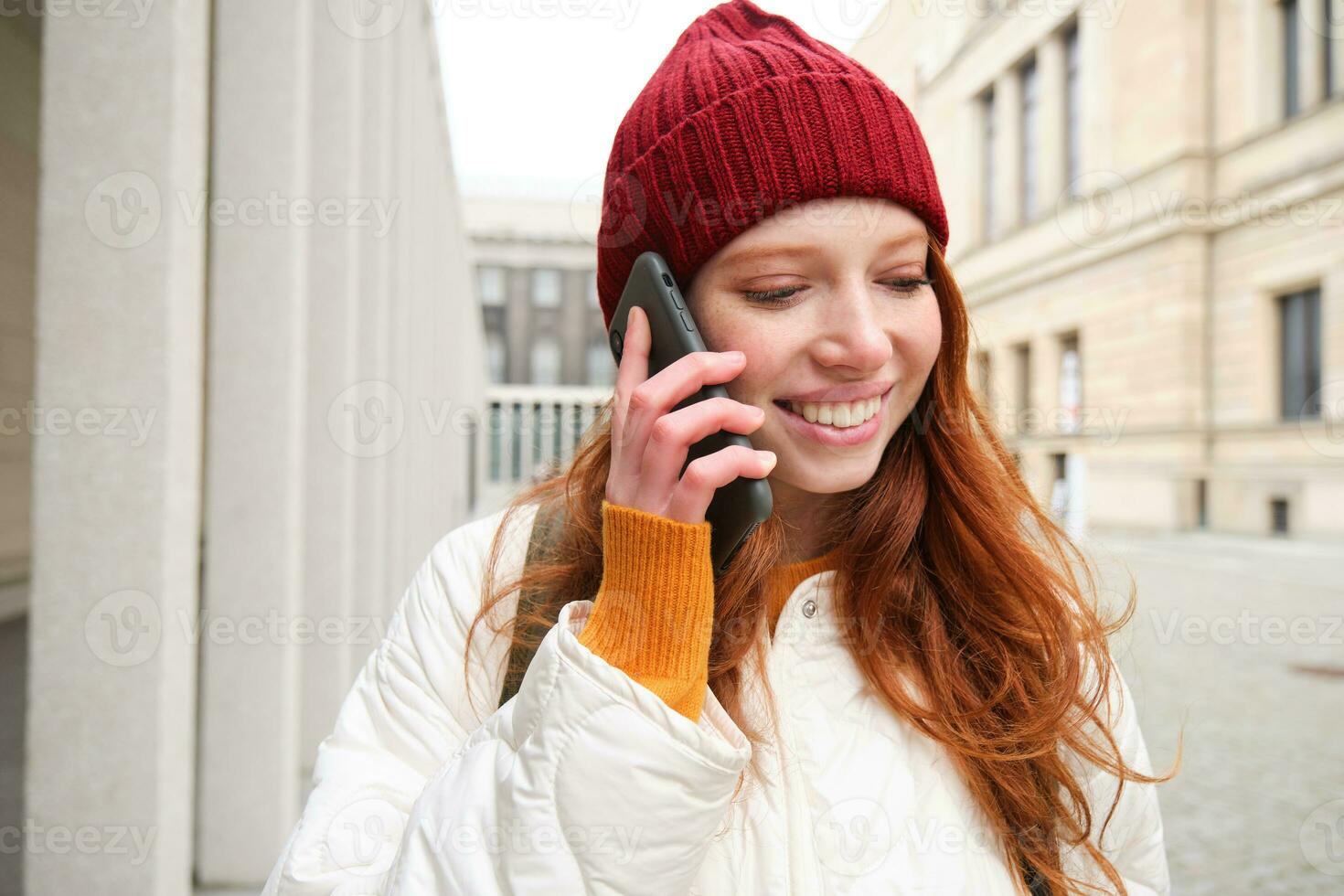 móvil banda ancha y gente. sonriente joven pelirrojo mujer camina en pueblo y negociaciones en móvil teléfono, vocación amigo en teléfono inteligente, utilizando Internet a hacer un llamada extranjero foto