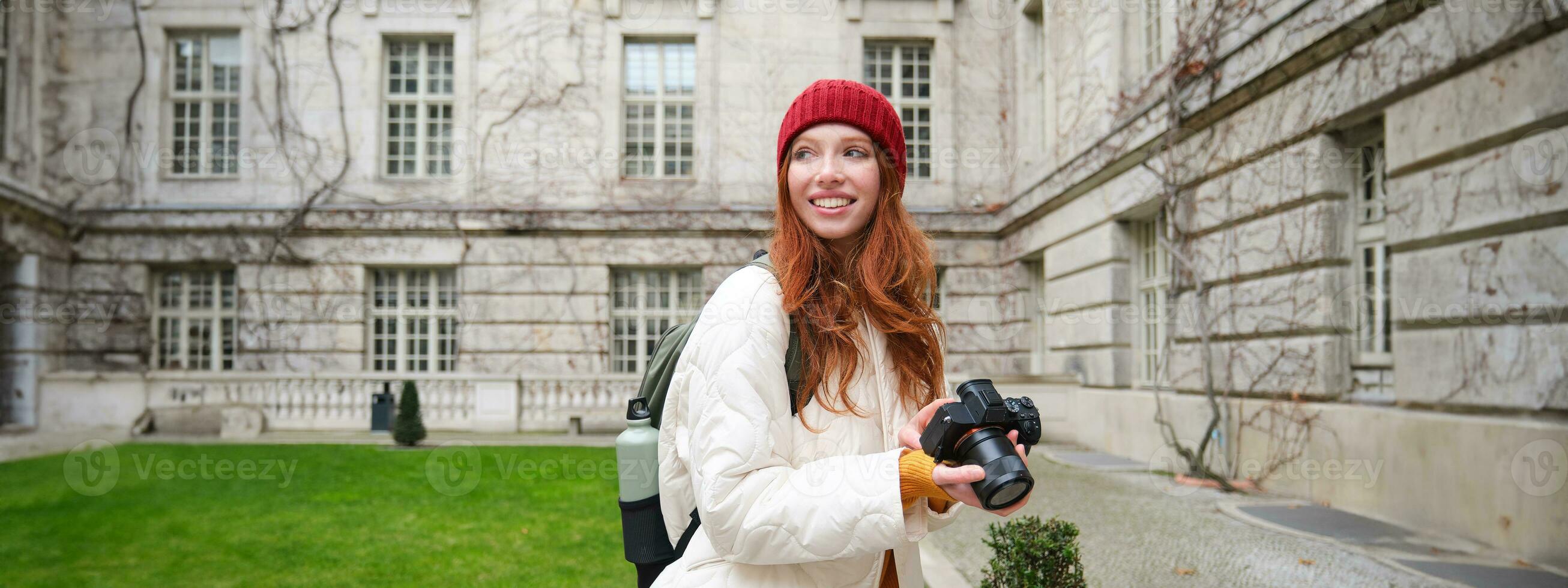 Happy redhead girl tourist, takes photos, photographer with professional camera walks around city and captures beautiful pictures photo