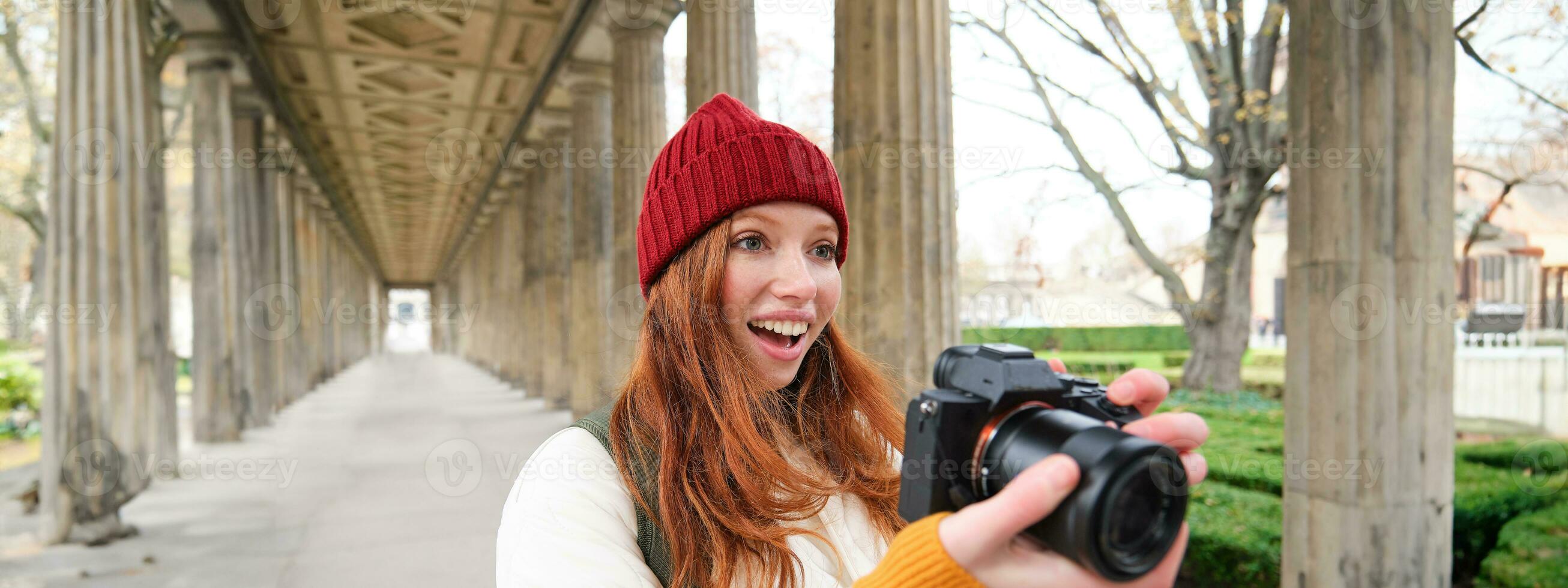 Smiling tourist photographer, takes picture during her trip, holds professional camera and makes photos