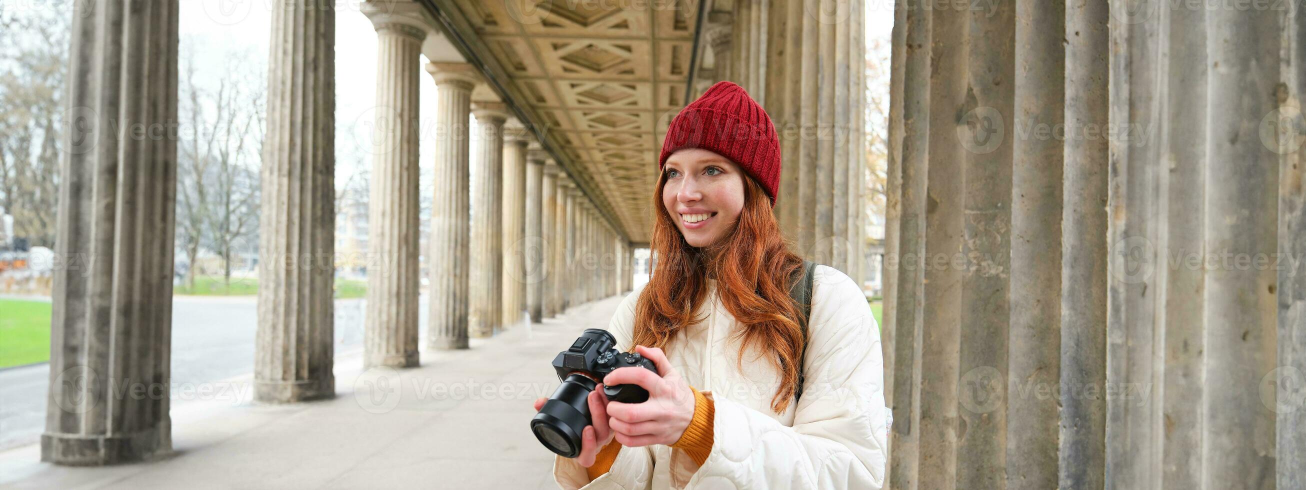 Smiling tourist photographer, takes picture during her trip, holds professional camera and makes photos