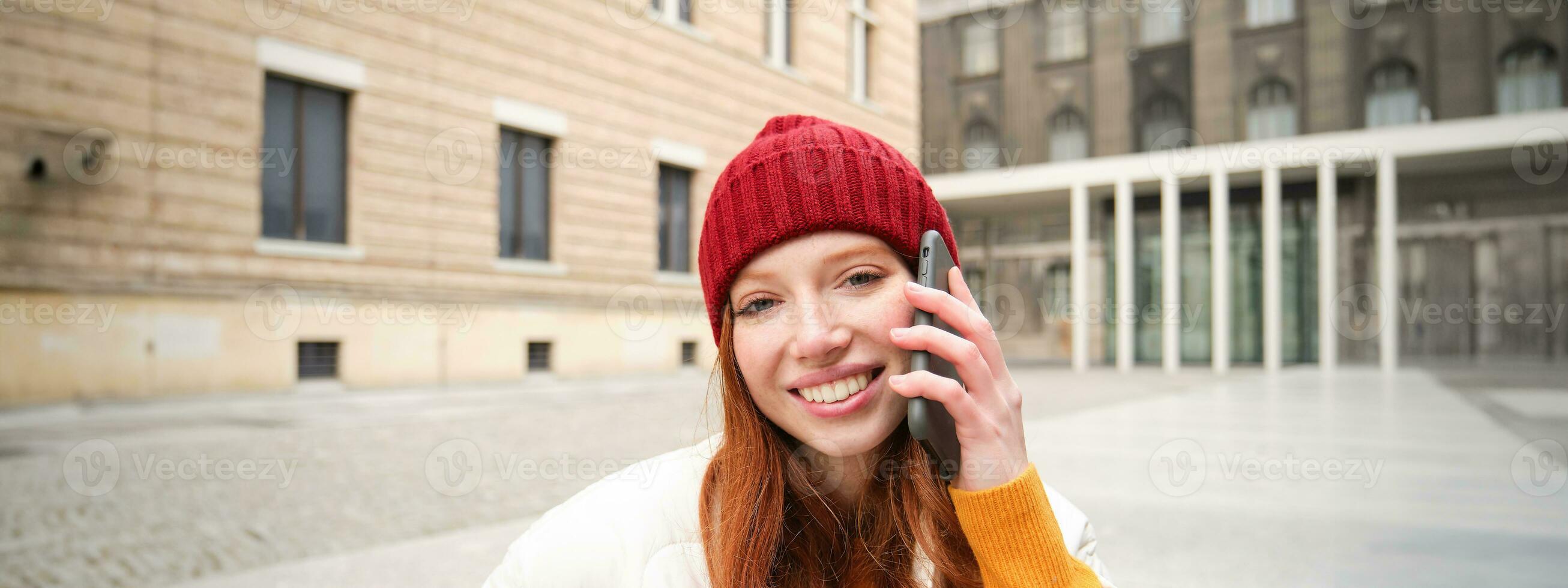 móvil conexión y personas concepto. contento pelirrojo mujer en sombrero, negociaciones en móvil teléfono, haciendo teléfono llamar, utilizando aplicación a llamada extranjero foto