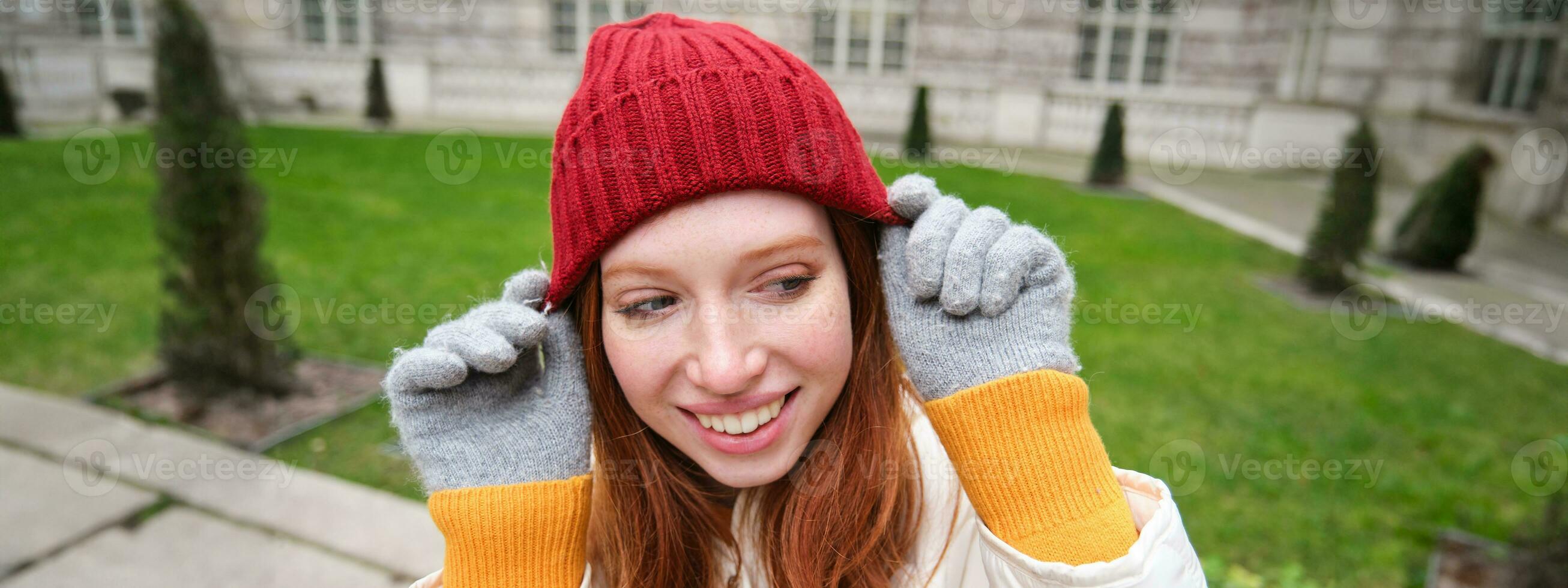 Cute girl student in red hat, warm gloves, sits in park, smiles and looks happy. photo