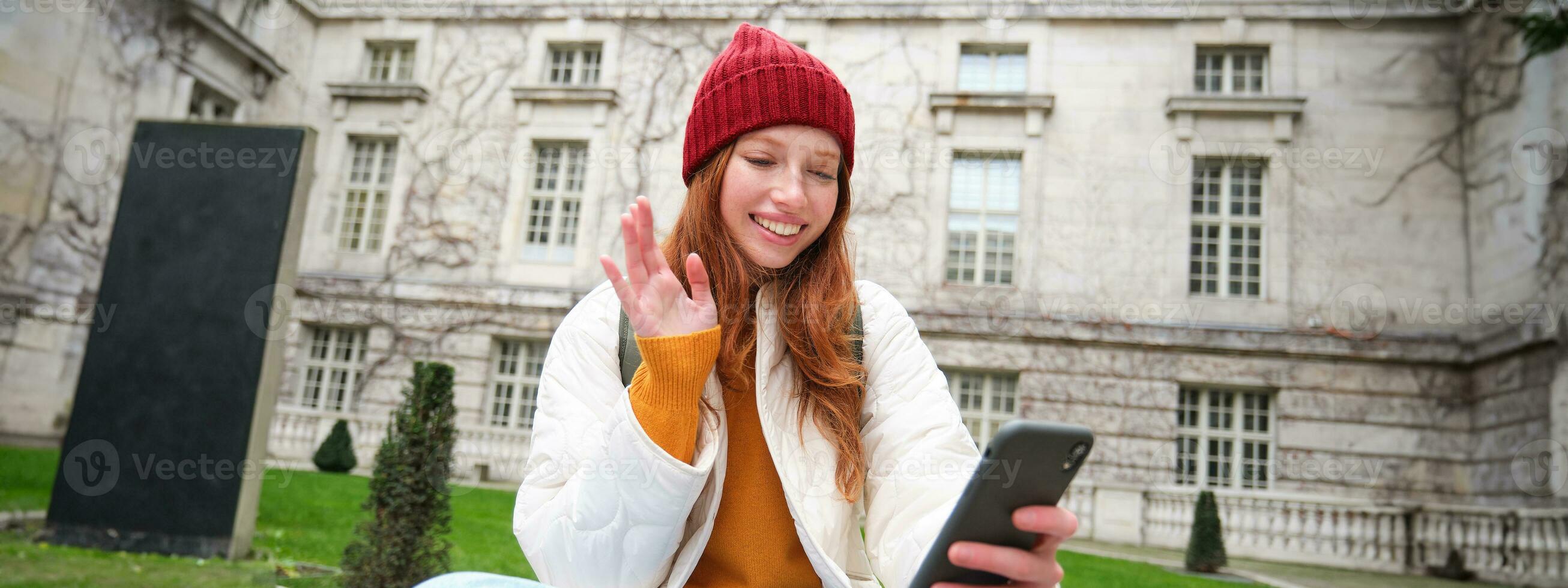 sonriente joven mujer dice Hola en vídeo charlar, conecta público Wifi en parque y negociaciones alguien en línea con teléfono inteligente aplicación foto