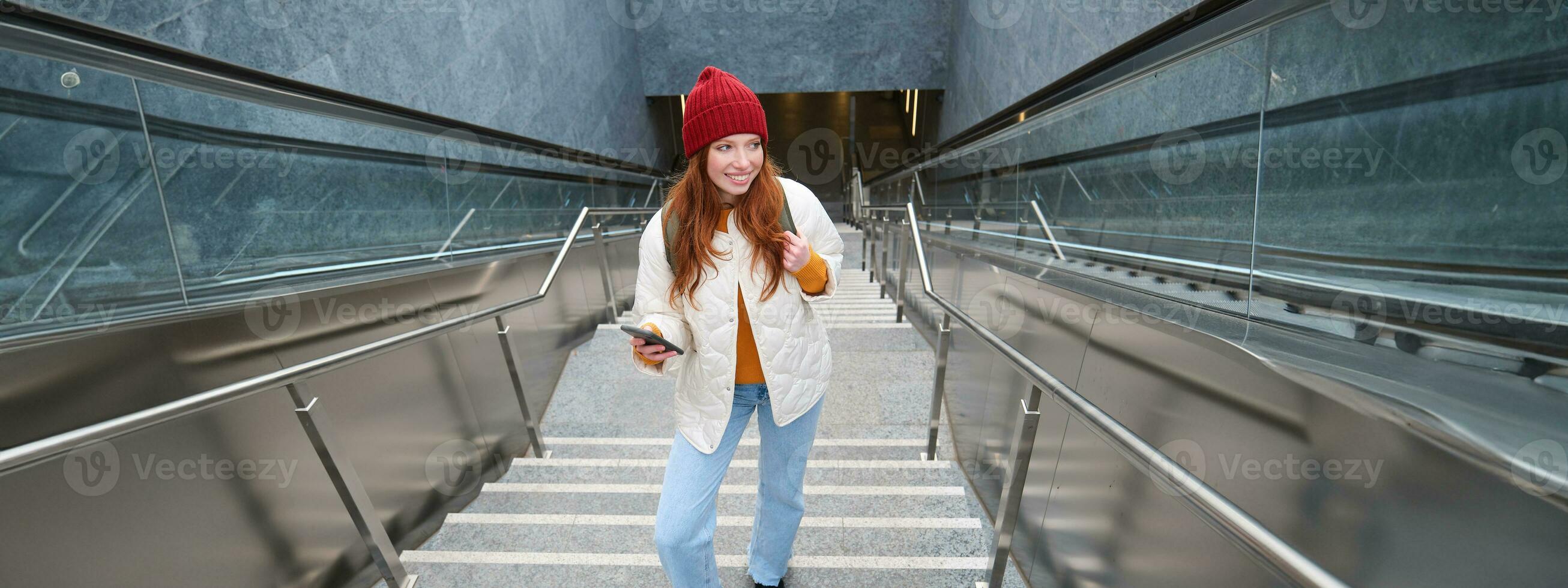 Outdoor shot of young woman plans route, follows map on smartphone app, goes up stairs with backpack and smiles photo