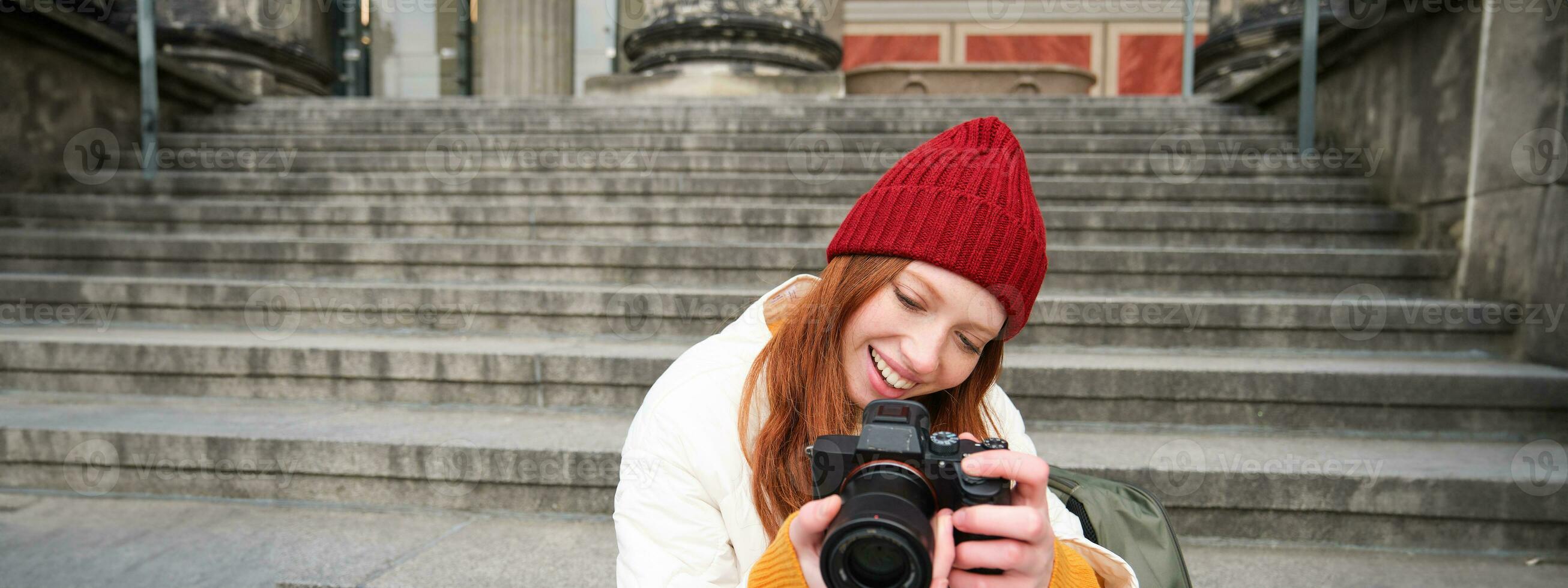Portrait of young photographer girl, sits on stairs with professional camera, takes photos outdoors, making lifestyle shooting