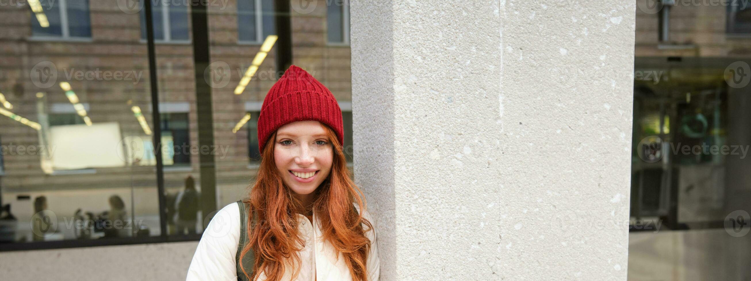 Beautiful redhead girl with smartphone, standing on street, holding mobile phone, using taxi app, connects to public wifi and uses internet, sends a text message photo