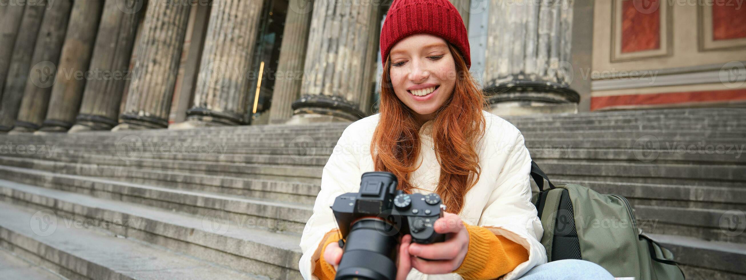 Portrait of young photographer girl, sits on stairs with professional camera, takes photos outdoors, making lifestyle shooting