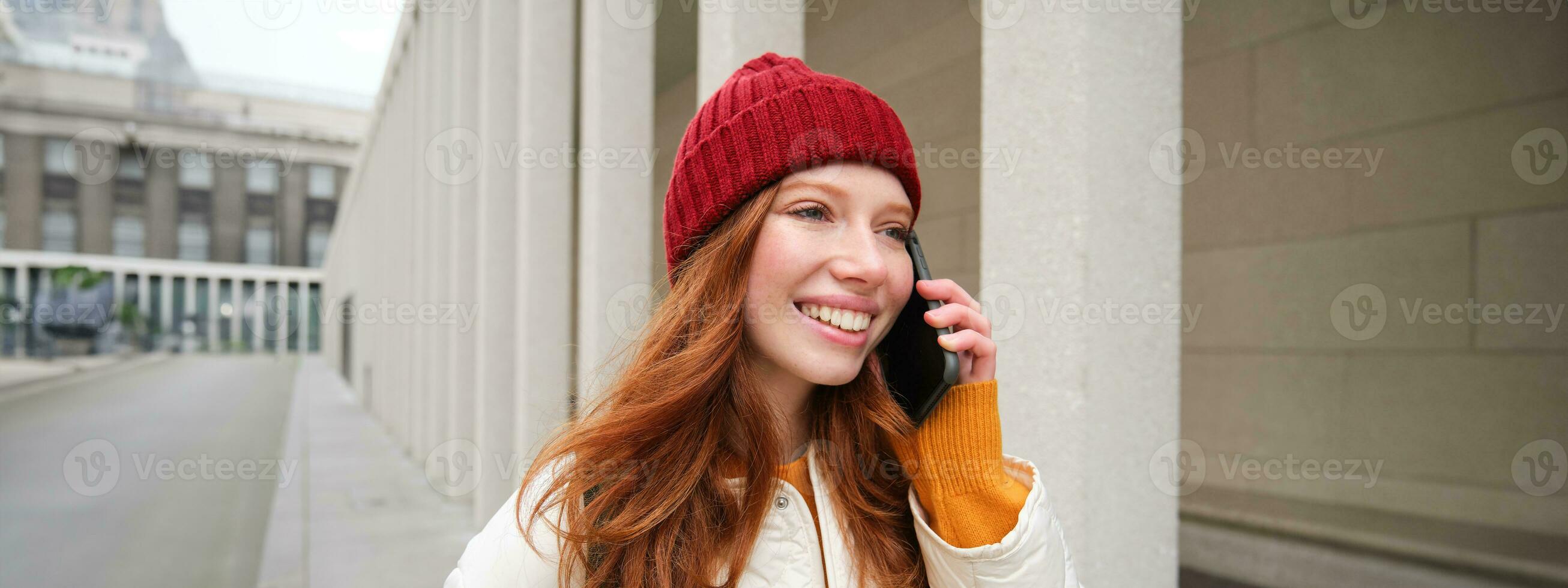 Happy redhead woman, girl with phone talks, has conversation on mobile app, uses internet to call abroad with smartphone app, laughing and smiling photo