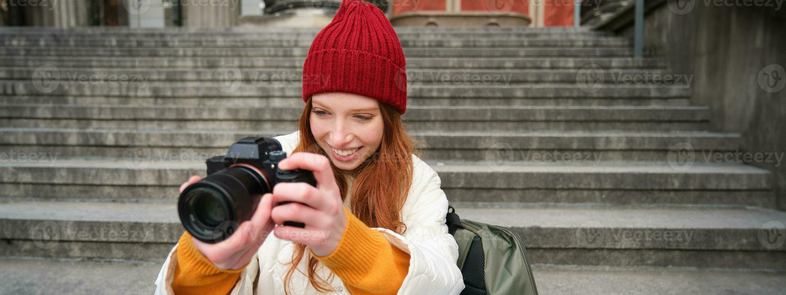 Portrait of young photographer girl, sits on stairs with professional camera, takes photos outdoors, making lifestyle shooting