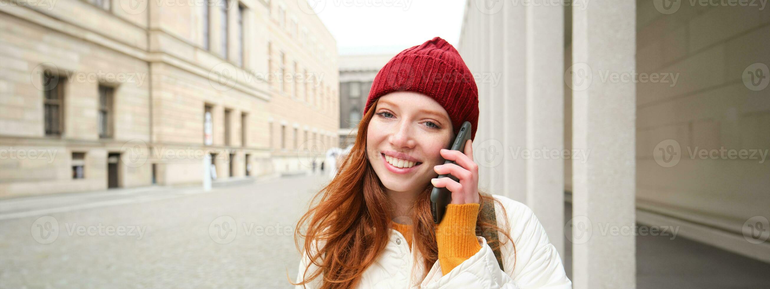 contento pelirrojo mujer, niña con teléfono negociaciones, tiene conversacion en móvil aplicación, usos Internet a llamada extranjero con teléfono inteligente aplicación, riendo y sonriente foto